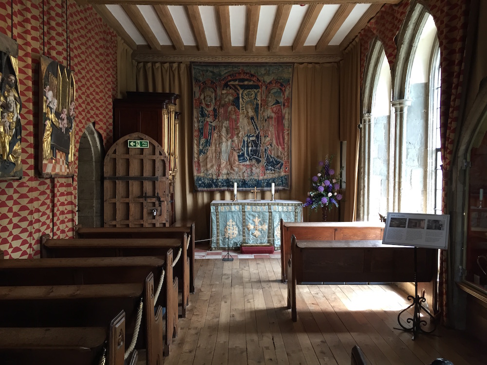 Kleine Kapelle mit 5 Sitzreihen. Ein wunderschöner alter Wandteppich hängt hinter dem Altar.