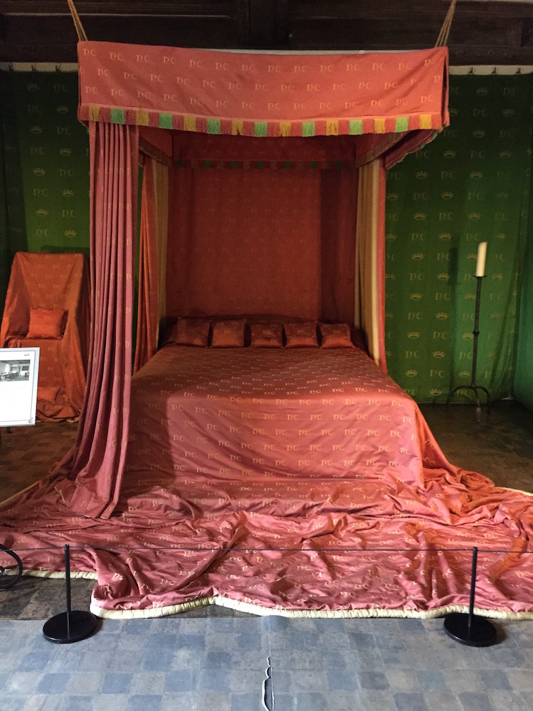 Ein großes Himmelbett mit einem roten Bettüberwurf, der bis auf den Boden fließt. Grüne Tapeten an den Wänden in Leeds Castle.