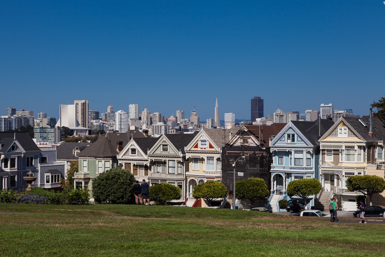 Bunt gestrichene Holzhäuser, im Hintergrund die Skyline von San Francisco